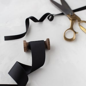 May include: A spool of black ribbon with a wooden spool and a pair of gold scissors with black ribbon wrapped around the handles.
