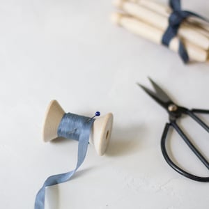 May include: A wooden spool of light blue ribbon with a pin, a pair of black scissors, and a bundle of wooden spools tied with blue ribbon.