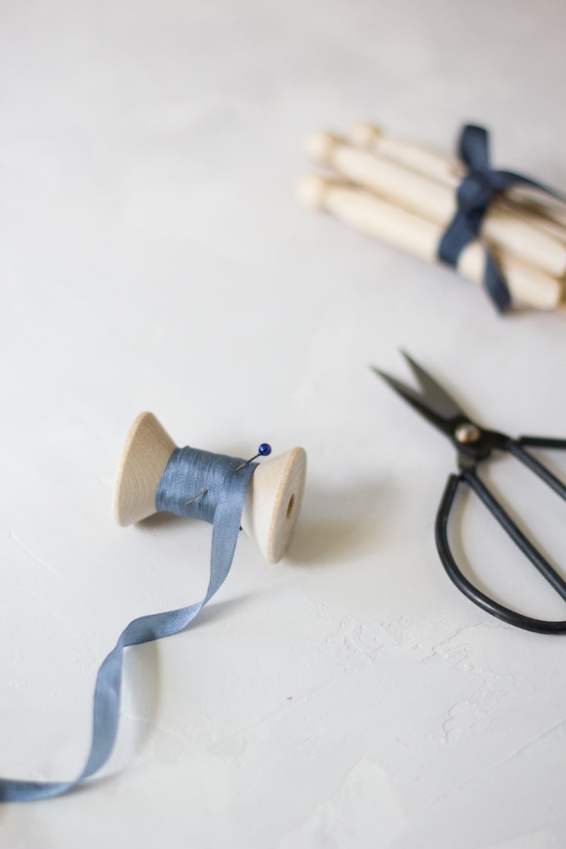May include: A wooden spool of light blue ribbon with a pin, a pair of black scissors, and a bundle of wooden spools tied with blue ribbon.