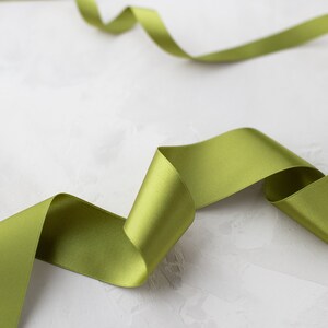 May include: A green satin ribbon is curled and twisted on a white textured background.