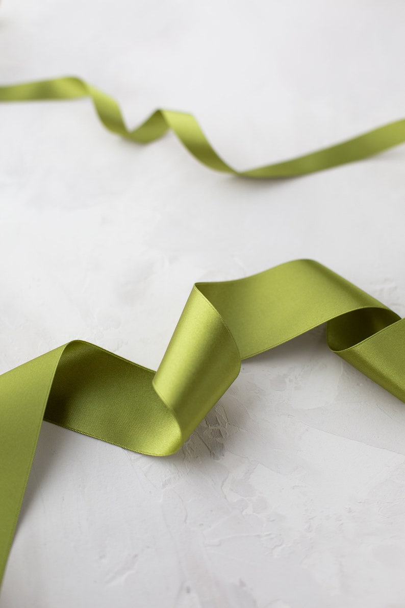 May include: A green satin ribbon is curled and twisted on a white textured background.