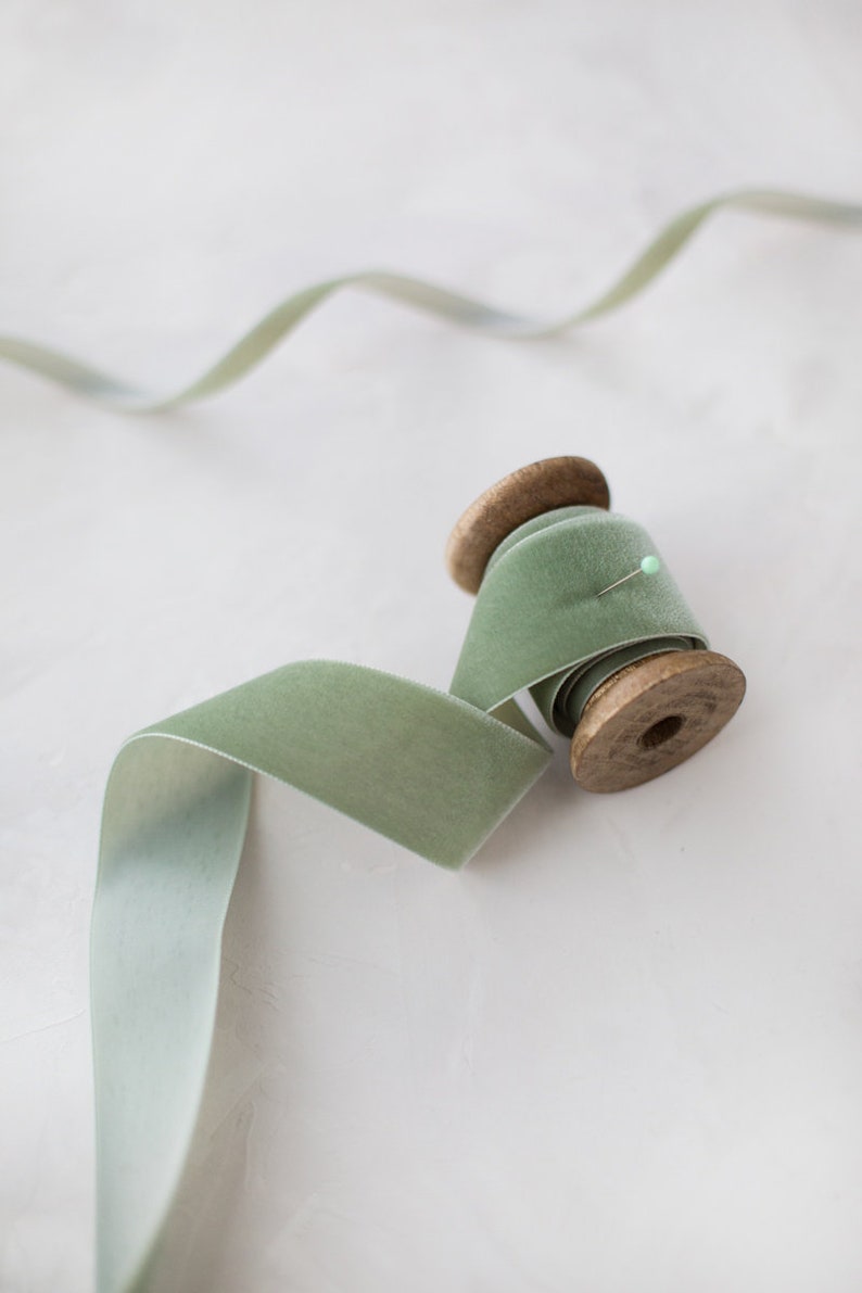 May include: A spool of sage green velvet ribbon with a wooden spool and a pin holding the ribbon in place.