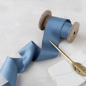 May include: A spool of light blue satin ribbon with a wooden spool and a gold feather quill pen.