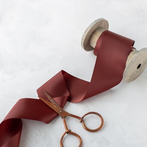 May include: A spool of maroon satin ribbon with a wooden spool and a pair of copper scissors.