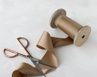 May include: A spool of gold satin ribbon with a wooden spool and a pair of silver scissors.