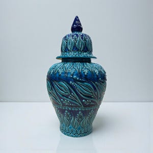 May include: A blue ceramic jar with a lid, featuring intricate embossed floral patterns. The jar has a bulbous body and a conical lid, all in shades of blue. The design includes detailed leaf and dot motifs, creating a textured surface.