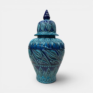 May include: A decorative ceramic jar with a lid, featuring a detailed floral pattern in shades of blue. The jar has a bulbous body and a conical lid, showcasing a glossy finish. The design includes raised relief elements.