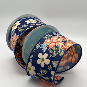 May include: A spool of navy blue ribbon featuring a repeating floral pattern with orange and white blossoms, green leaves, and small berries. The ribbon has a textured, ribbed surface and is wrapped around a circular cardboard core with a label.