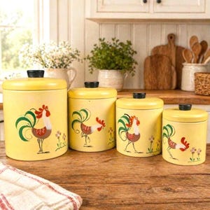 May include: A set of four yellow kitchen canisters with black lids. Each canister features a hand-painted rooster design with green, red, and brown accents. The canisters are arranged on a wooden surface.