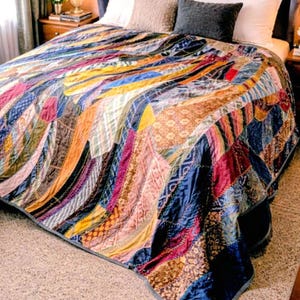 May include: A colorful patchwork quilt with a variety of fabrics and patterns. The quilt features a mix of colors, including blue, orange, red, and gold. The quilt is on a bed with white pillows and a gray headboard. The quilt is a decorative bedding item.