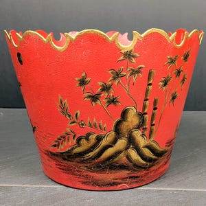 May include: A bright red planter with a scalloped rim featuring a gold painted edge. The exterior surface has a crackled texture and is decorated with black and gold painted illustrations of bamboo stalks, rocks, and leafy foliage.