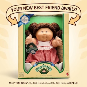 May include: A Cabbage Patch Kids doll with brown yarn hair in pigtails, wearing a red and white checkered dress with a white collar. The doll is inside a box labeled 15th Anniversary Special Edition, with text reading YOUR NEW BEST FRIEND AWAITS!
