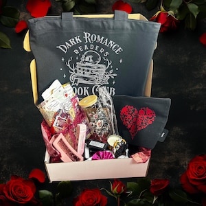 May include: A gift box with a dark romance theme, featuring a gray tote bag with "Dark Romance Readers Book Club" text and skull graphic. Includes a black pouch with a red skull heart design, a glass jar, and other items, surrounded by red roses.