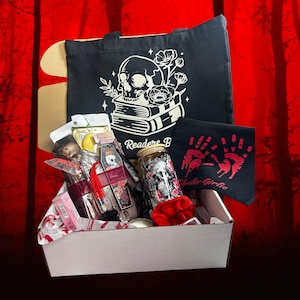 May include: A gift box with a black tote bag featuring a skull and floral design, a black hand towel with red handprints, and various items. The box contains a jar with a skull design, and other items.