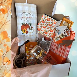 May include: A gift box filled with fall-themed items. Includes a tea towel with "Farm Fresh Pumpkin Patch" text, a pumpkin-patterned pouch, a glass with "Pumpkin Spice" text, and other decorative items. The box is open, revealing the contents.