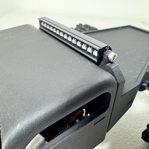 May include: A black, rectangular light bar with multiple small LED lights mounted on a black, angular structure. The structure appears to be part of a larger, possibly robotic, device. The image is a close-up.