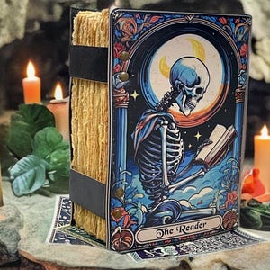 Peut inclure: Un livre rectangulaire avec une tranche en papier &eacute;pais et textur&eacute; brun clair, maintenu par des sangles noires. La couverture illustre un squelette lisant un livre sous un croissant de lune, avec le texte The Reader imprim&eacute; en bas.