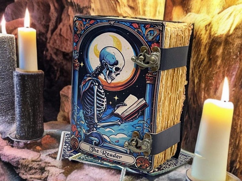 Peut inclure: Un livre rectangulaire intitul&eacute; The Reader pr&eacute;sentant une illustration color&eacute;e d'un squelette lisant un livre sous un croissant de lune. Le livre a une texture de pages vieillies et est fix&eacute; par deux fermoirs en m&eacute;tal fonc&eacute; sur le c&ocirc;t&eacute;.