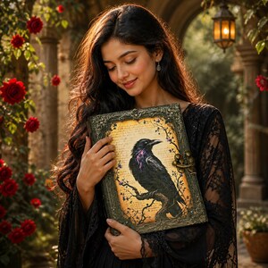 May include: A decorative journal with a raven illustration. The journal features a black raven perched on a branch, with purple accents, set against a vintage parchment background. The cover has an ornate, dark frame with a clasp.