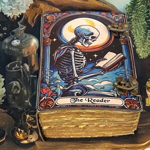 Peut inclure: Un livre rectangulaire &agrave; couverture rigide pr&eacute;sentant une illustration color&eacute;e d'un squelette lisant un livre sous une lune. La couverture poss&egrave;de deux fermoirs m&eacute;talliques couleur laiton sur le c&ocirc;t&eacute; droit. Les pages sont &eacute;paisses et beiges.