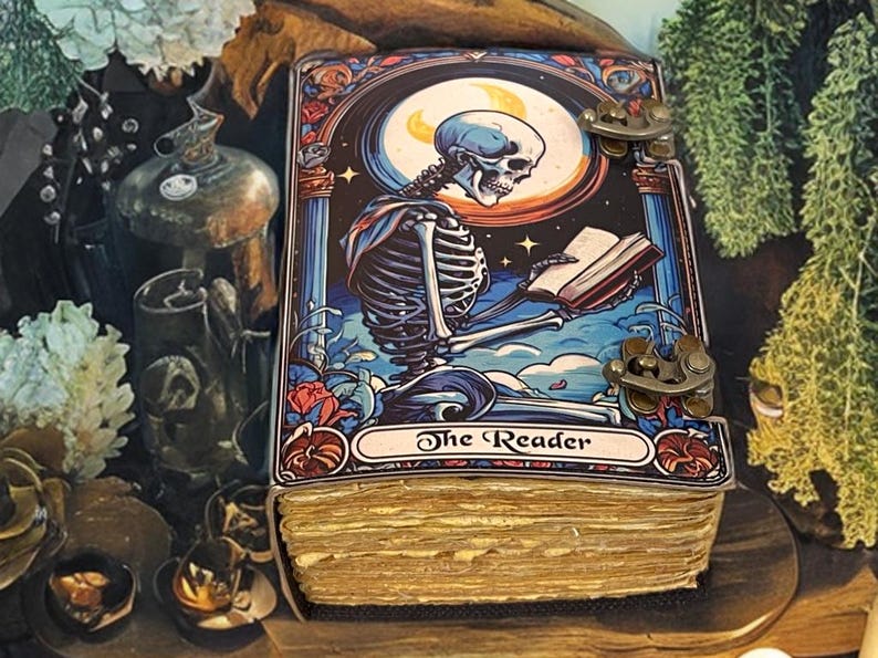 Peut inclure: Un livre rectangulaire &agrave; couverture rigide pr&eacute;sentant une illustration color&eacute;e d'un squelette lisant un livre sous une lune. La couverture poss&egrave;de deux fermoirs m&eacute;talliques couleur laiton sur le c&ocirc;t&eacute; droit. Les pages sont &eacute;paisses et beiges.