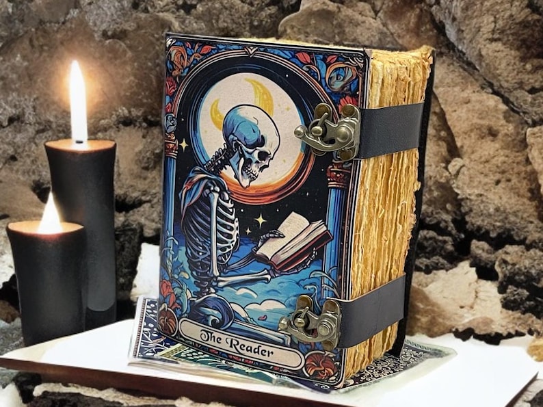 Peut inclure: Un livre reli&eacute; intitul&eacute; The Reader avec une illustration color&eacute;e d'un squelette lisant un livre sous un croissant de lune. Le livre a des pages vieillies et est maintenu par deux sangles noires avec des fermoirs en m&eacute;tal laitonn&eacute;.