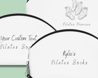 May include: White cosmetic bags with black zips and wrist straps. One bag features a sketch of socks and the text "Pilates Princess." Another bag says "Kylie's Pilates Socks." The third bag says "Your Custom Text Pilates Socks."