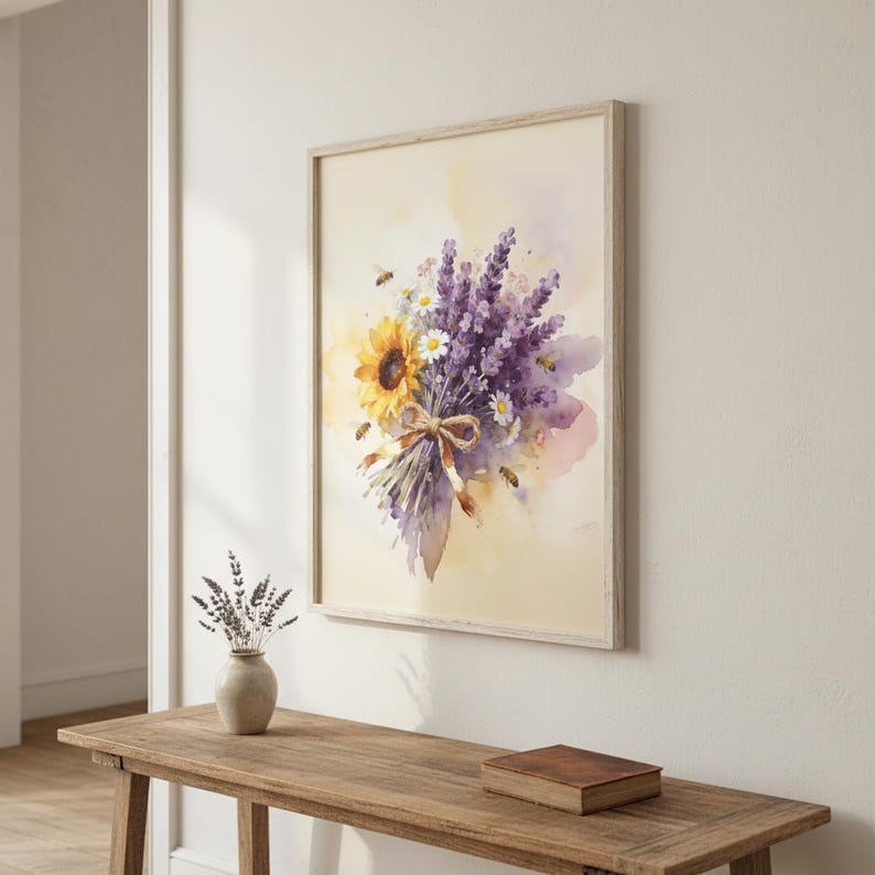 May include: Watercolour print of a bouquet featuring a sunflower, lavender, and daisies, tied with a brown ribbon. The artwork is framed in a light wood frame and hangs on a cream-coloured wall. Bees are scattered around the flowers.