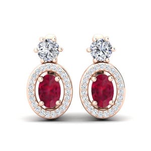 May include: A pair of rose gold earrings. Each earring has a large, oval-cut, deep red gemstone surrounded by a halo of small, clear gemstones. A smaller, round, clear gemstone sits at the top of each earring.