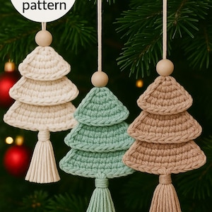 Può includere: Tre decorazioni per l'albero di Natale all'uncinetto fatte a mano in crema, verde menta e marrone, ciascuna con una perla di legno e nappa. Il testo "Digital crochet pattern" è in un cerchio bianco. Le decorazioni sono appese a rami di sempreverdi.