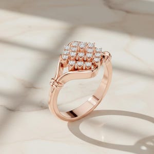 K&ouml;nnte beinhalten: Ros&eacute;goldener Ring mit einer Ansammlung kleiner, runder Diamanten. Der Ring hat ein einzigartiges Design mit einem gedrehten Detail in der N&auml;he des Bandes und einer geschwungenen, offenen Fassung f&uuml;r die Diamanten. Der Ring ist vor einem hellen Hintergrund platziert.