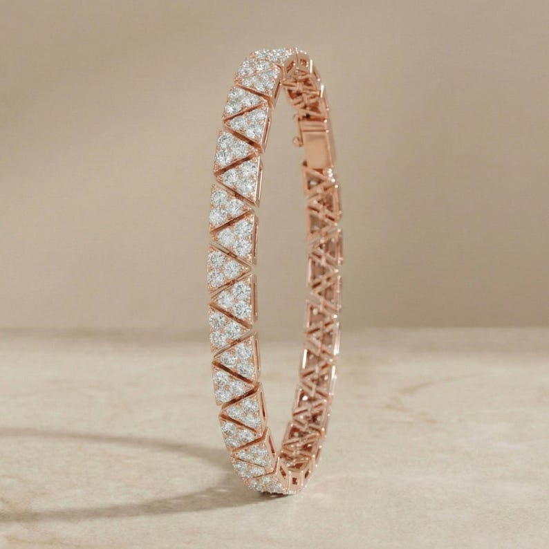 May include: Rose gold bracelet with a geometric design. The bracelet features triangular sections encrusted with small, sparkling white stones. The clasp is visible on the right side, and the bracelet is set against a neutral background.