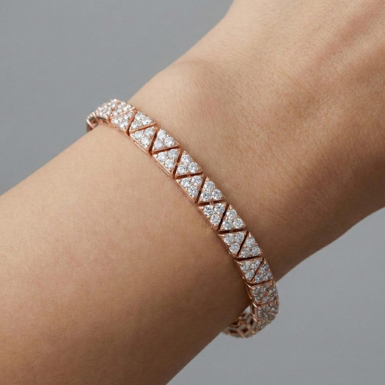 May include: Rose gold bracelet with a geometric design. The bracelet features a series of triangular links, each encrusted with small, sparkling white gemstones. The bracelet is shown on a wrist against a neutral background.