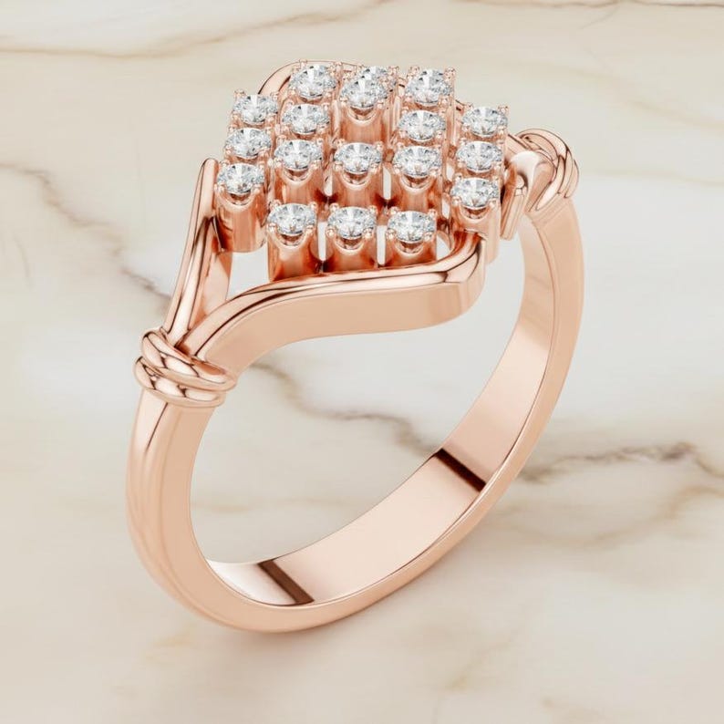 K&ouml;nnte beinhalten: Ros&eacute;goldener Ring mit einer Ansammlung kleiner, runder, klarer Edelsteine in quadratischer Form. Das Band hat eine glatte, polierte Oberfl&auml;che mit einem Knotendesign an der Seite. Der Ring wird auf einer Marmoroberfl&auml;che pr&auml;sentiert.