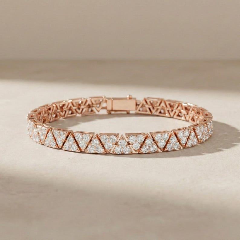 May include: Rose gold bracelet featuring a geometric design of interconnected triangles. Each triangle is encrusted with small, sparkling white stones. The bracelet has a secure clasp closure, showcasing a blend of modern and elegant design.