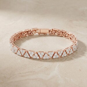 May include: Rose gold bracelet featuring a repeating pattern of triangular shapes, each encrusted with small, sparkling stones. The bracelet has a secure clasp closure and is displayed on a neutral background.