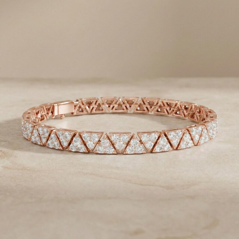 May include: Rose gold bracelet featuring a repeating triangular design. Each triangle is encrusted with small, sparkling white stones. The bracelet is displayed on a neutral, light-colored surface.