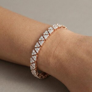 May include: Rose gold bracelet featuring a repeating pattern of triangular links, each encrusted with small, sparkling white gemstones. The bracelet is shown on a wrist against a neutral background.