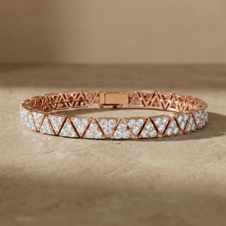 May include: Rose gold bracelet featuring a repeating pattern of triangular shapes, each encrusted with small, sparkling gemstones. The bracelet is designed with a secure clasp and rests on a neutral-toned surface, showcasing its elegant design.