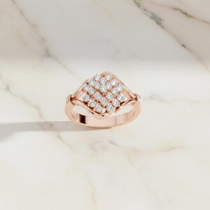 K&ouml;nnte beinhalten: Ros&eacute;goldener Ring mit einem quadratischen Cluster aus kleinen, runden Diamanten. Der Ring hat ein filigranes, offenes Design und ein glattes Band. Die Diamanten sind eng beieinander gesetzt und erzeugen einen funkelnden Effekt. Der Ring wird auf einer wei&szlig;en Marmoroberfl&auml;che pr&auml;sentiert.