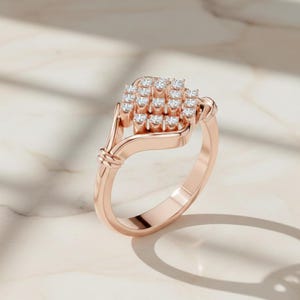 K&ouml;nnte beinhalten: Ros&eacute;goldener Ring mit einer Ansammlung kleiner, funkelnder Diamanten. Der Ring hat ein zartes, geschwungenes Design mit einem geflochtenen Detail in der N&auml;he des Bandes. Der Ring ist auf einer hellen, marmor&auml;hnlichen Oberfl&auml;che platziert.