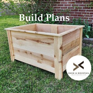 May include: A rectangular wooden planter box with the text "Build Plans" in white. The box is made of light-coloured wood and sits on a grassy surface. The Duck & Dovetail woodworking logo is in the bottom right corner.