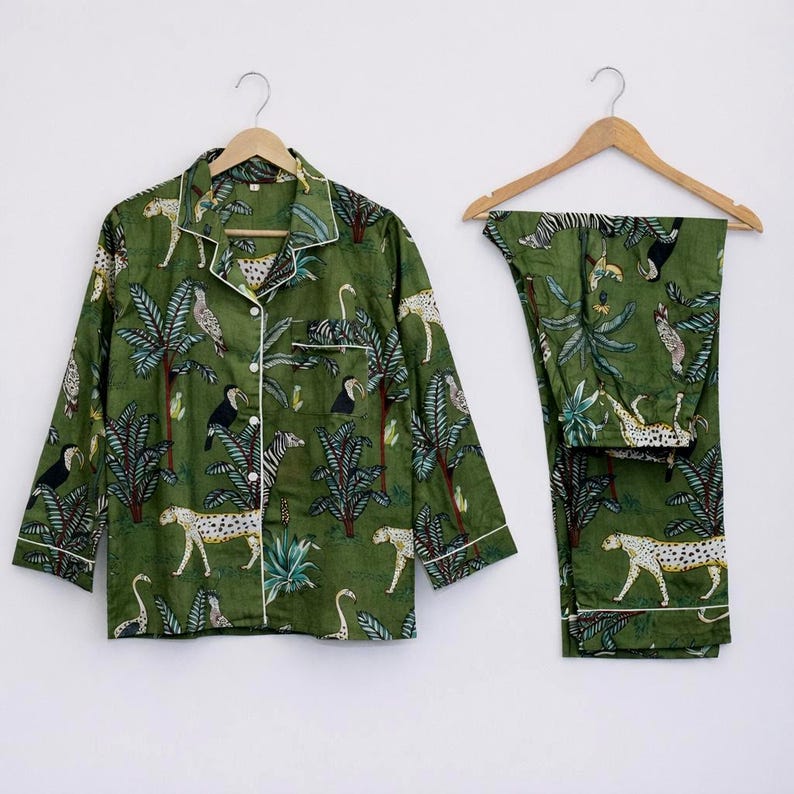 Puede incluir: Conjunto de pijama verde con estampado de jungla. El conjunto incluye una camisa con botones y pantalones a juego. El estampado presenta leopardos, cebras, tucanes y palmeras. La camisa tiene ribetes blancos y est&aacute; colgada.