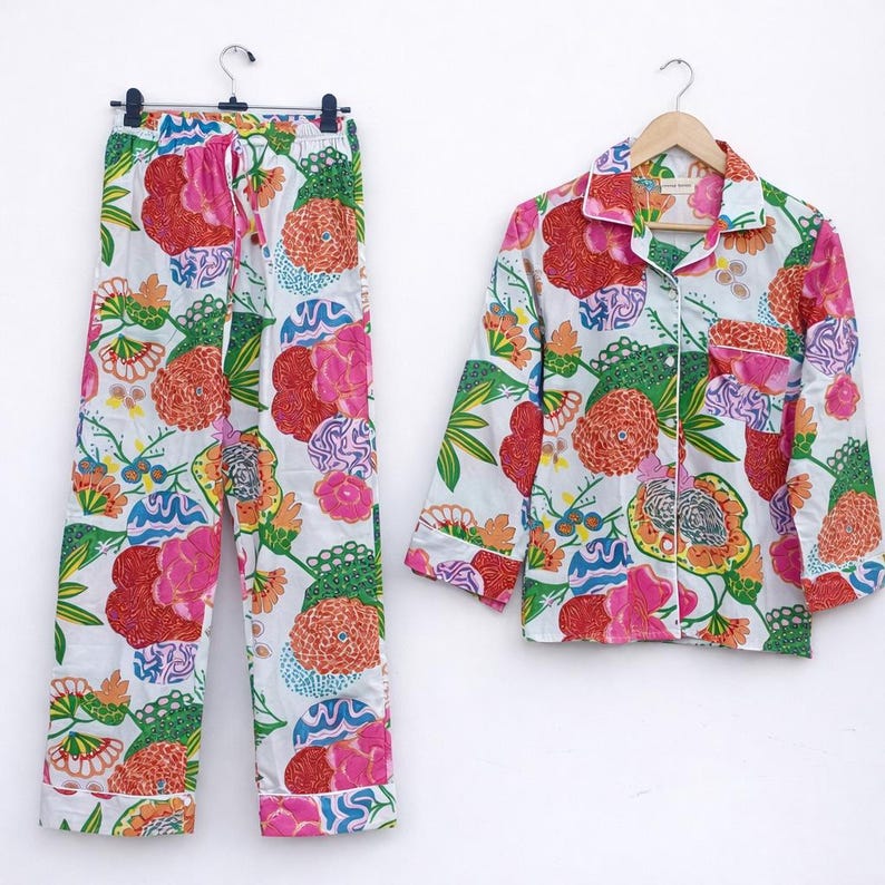 Puede incluir: Un conjunto de pijama a juego con un estampado floral en tonos rosa, naranja, verde y azul sobre un fondo blanco. El conjunto incluye una camisa de manga larga con botones y pantalones con cintura con cord&oacute;n. Los pijamas est&aacute;n colgados.