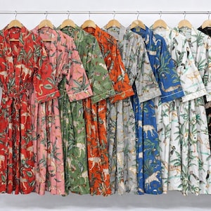May include: A collection of colorful, patterned robes hanging on a clothing rack. The robes feature various animal and plant designs in shades of red, pink, green, orange, gray, blue, white, and black. Each robe has a matching belt and white trim.