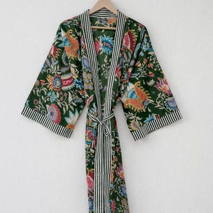 May include: A dark green floral print robe with a striped trim and belt. The robe features a colorful floral pattern with red, blue, yellow, and pink accents. The trim and belt are white with black stripes. The robe is hanging on a wooden hanger.