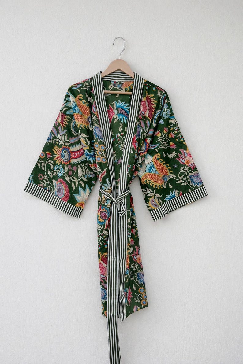 May include: A dark green floral print robe with a striped trim and belt. The robe features a colorful floral pattern with red, blue, yellow, and pink accents. The trim and belt are white with black stripes. The robe is hanging on a wooden hanger.