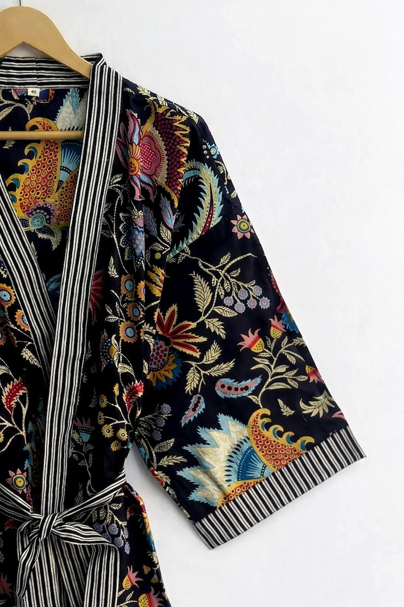 May include: A dark blue robe with a vibrant floral pattern in red, yellow, blue, and green. The robe features black and white striped trim on the edges and a matching tie belt. The sleeves are three-quarter length.