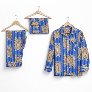 May include: Blue striped pajama set with a tiger print. The set includes a long-sleeved button-down shirt, pants, and a matching pouch, all hanging on wooden hangers. The tiger print is in shades of tan and brown.