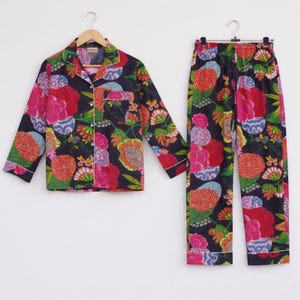 Puede incluir: Conjunto de pijama de dos piezas con un fondo azul marino oscuro y un vibrante estampado floral. La camisa abotonada de manga larga y los pantalones a juego presentan flores rojas, rosas, naranjas, verdes y azules.